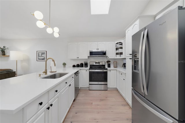 kitchen featuring appliances with stainless steel finishes, decorative light fixtures, white cabinetry, sink, and light wood-type flooring