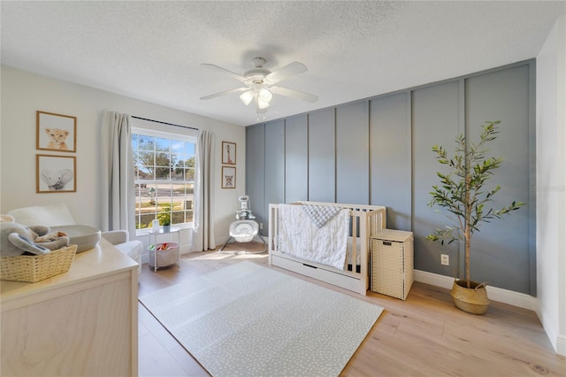 bedroom with ceiling fan, light hardwood / wood-style flooring, a nursery area, and a textured ceiling