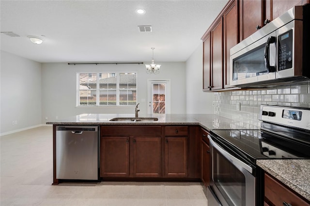 kitchen with sink, stainless steel appliances, light stone counters, decorative backsplash, and decorative light fixtures