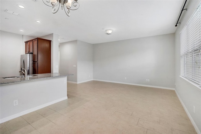 kitchen with light stone countertops, sink, stainless steel fridge, and an inviting chandelier