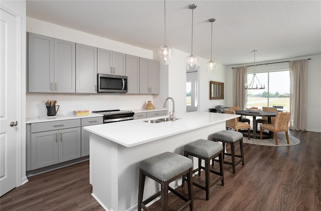 kitchen with pendant lighting, sink, appliances with stainless steel finishes, a kitchen island with sink, and gray cabinetry