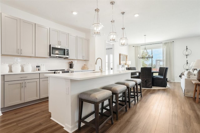 kitchen featuring gray cabinetry, hanging light fixtures, backsplash, and an island with sink