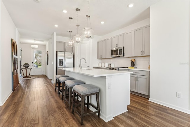 kitchen with a kitchen bar, sink, gray cabinets, an island with sink, and stainless steel appliances