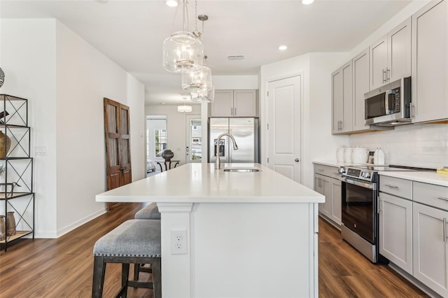 kitchen featuring appliances with stainless steel finishes, an island with sink, sink, gray cabinetry, and decorative backsplash