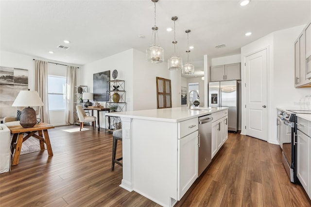 kitchen featuring sink, hanging light fixtures, stainless steel appliances, and an island with sink