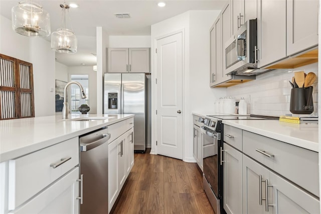 kitchen with dark wood-type flooring, gray cabinets, backsplash, stainless steel appliances, and decorative light fixtures