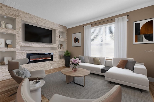 living room with ornamental molding, a stone fireplace, hardwood / wood-style floors, and built in shelves