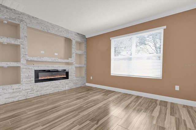 unfurnished living room with built in shelves, ornamental molding, and a stone fireplace