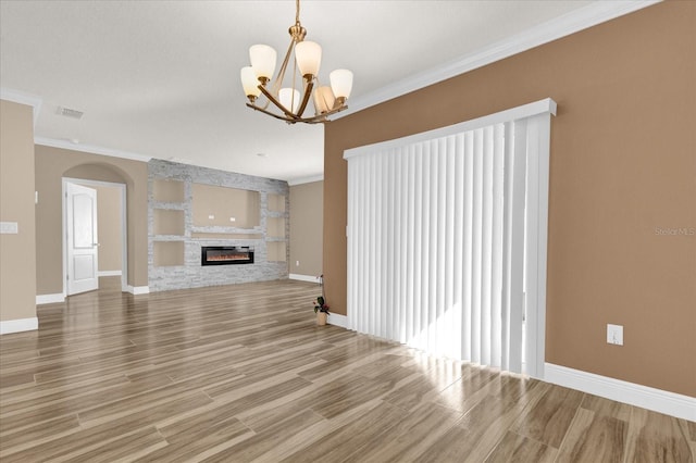 unfurnished living room featuring crown molding, wood-type flooring, a stone fireplace, and an inviting chandelier