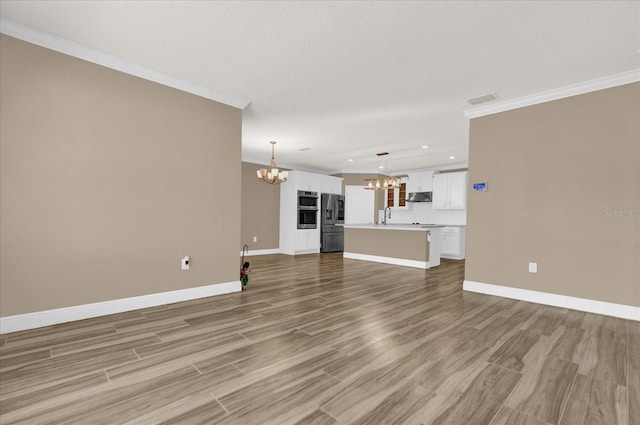 unfurnished living room with hardwood / wood-style flooring, ornamental molding, sink, and a notable chandelier