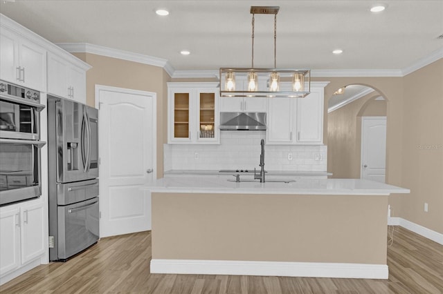 kitchen featuring stainless steel appliances, decorative light fixtures, an island with sink, and wall chimney range hood