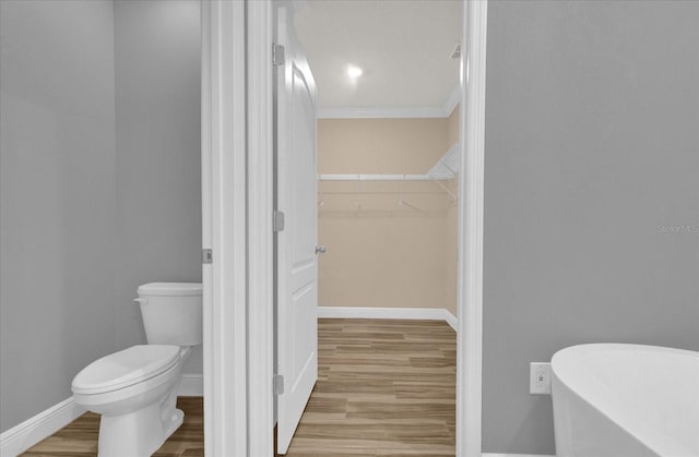 bathroom with crown molding, wood-type flooring, toilet, and a washtub