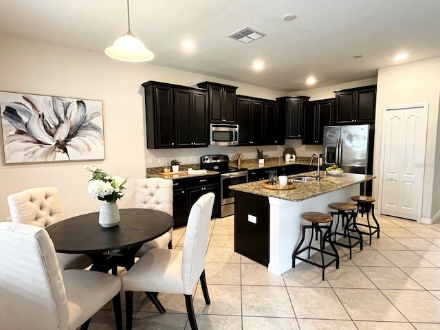 kitchen featuring light tile patterned flooring, sink, decorative light fixtures, stainless steel appliances, and a kitchen island with sink