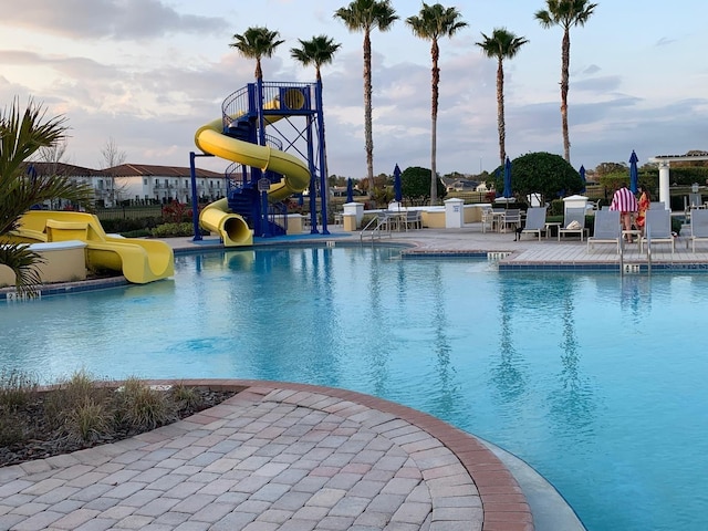 view of pool with a water slide, a playground, and a patio area