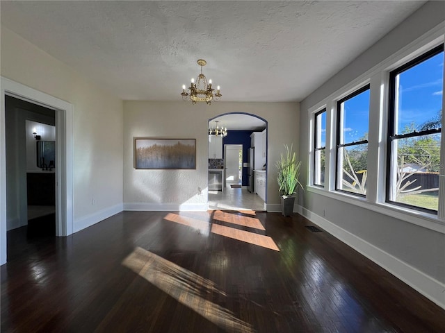 empty room with an inviting chandelier, dark wood-type flooring, and a textured ceiling