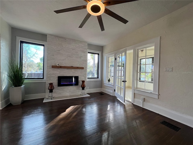 unfurnished living room with dark hardwood / wood-style flooring, a stone fireplace, plenty of natural light, and a textured ceiling