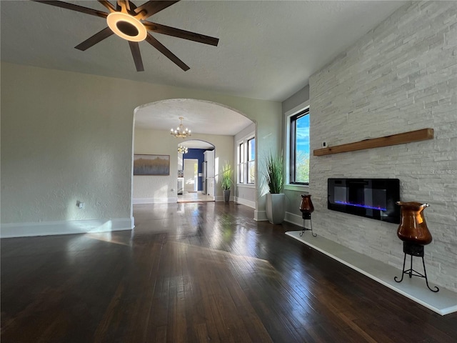 unfurnished living room with dark hardwood / wood-style floors, a stone fireplace, ceiling fan with notable chandelier, and a textured ceiling