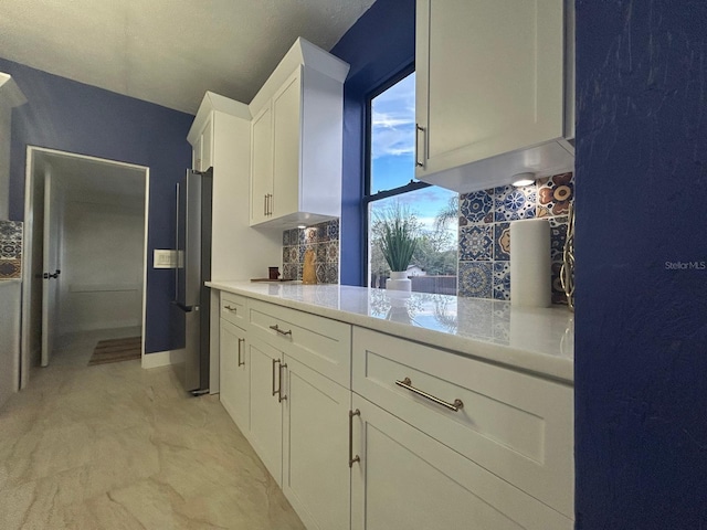 kitchen featuring white cabinetry, decorative backsplash, light stone countertops, and stainless steel refrigerator