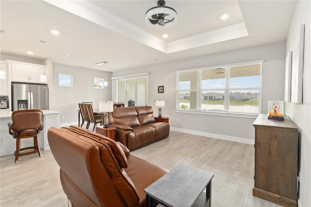 living room with a raised ceiling, crown molding, and light wood-type flooring