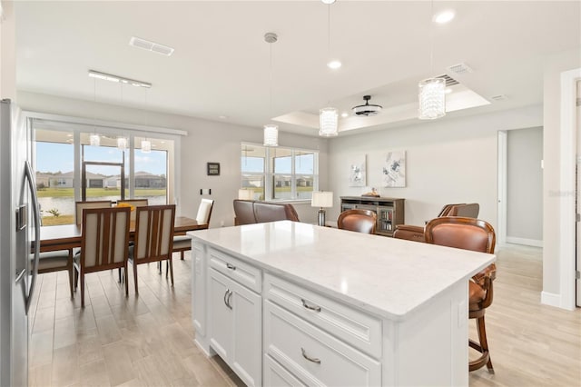 kitchen featuring pendant lighting, white cabinetry, stainless steel fridge, a kitchen bar, and a center island