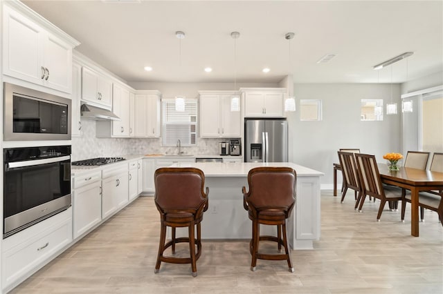 kitchen featuring hanging light fixtures, a kitchen island, appliances with stainless steel finishes, and white cabinets