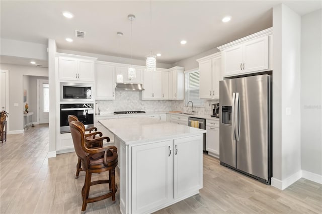 kitchen with white cabinetry, appliances with stainless steel finishes, decorative light fixtures, and a center island