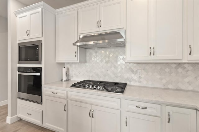 kitchen featuring exhaust hood, white cabinets, stainless steel appliances, light stone countertops, and backsplash