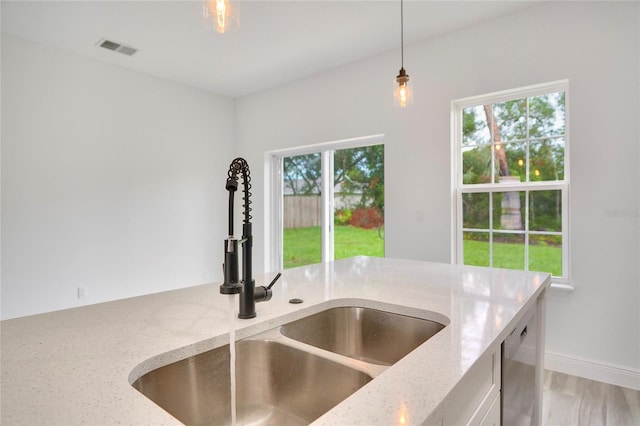 kitchen featuring a sink, visible vents, baseboards, hanging light fixtures, and light stone countertops