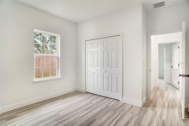 unfurnished bedroom with light wood finished floors, visible vents, baseboards, and a closet