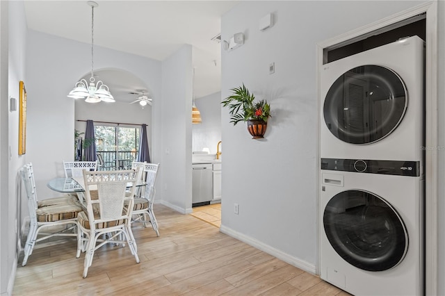 laundry area featuring stacked washing maching and dryer, ceiling fan with notable chandelier, and light hardwood / wood-style floors