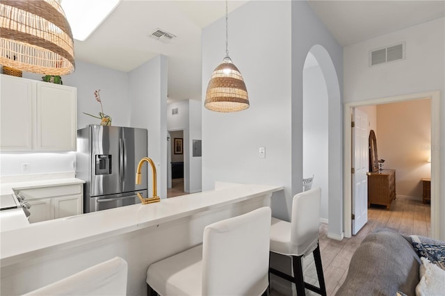 kitchen with decorative light fixtures, white cabinets, stainless steel fridge, a kitchen bar, and light wood-type flooring