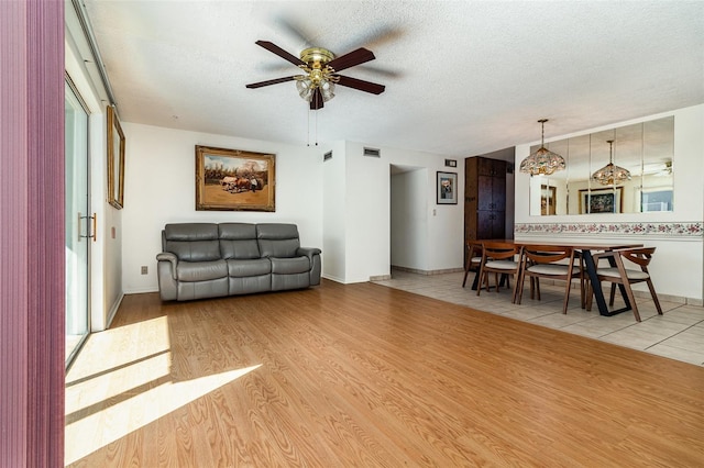 living room with ceiling fan, light hardwood / wood-style flooring, and a textured ceiling