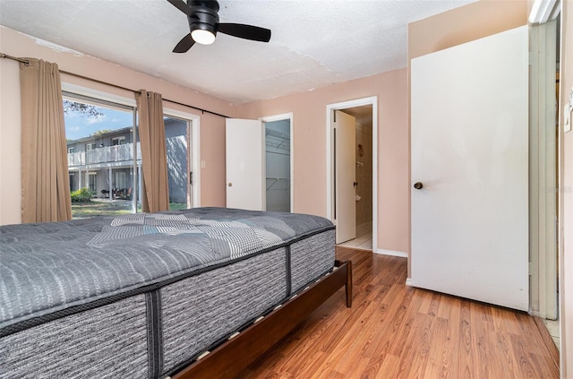 bedroom with a walk in closet, access to outside, ceiling fan, light hardwood / wood-style floors, and a textured ceiling