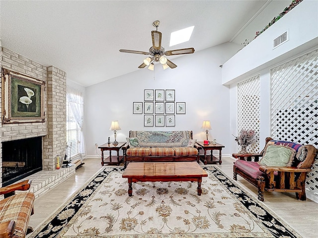 living room featuring ceiling fan, a fireplace, light wood-type flooring, and lofted ceiling with skylight