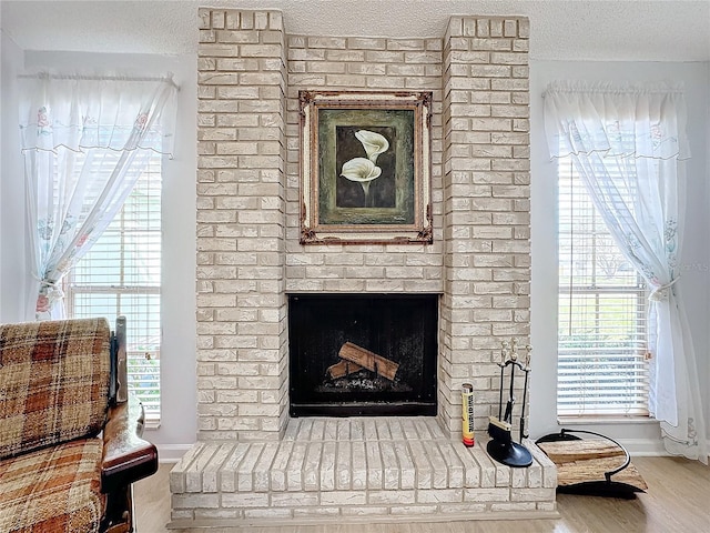 living area featuring wood-type flooring, a brick fireplace, a textured ceiling, and a wealth of natural light