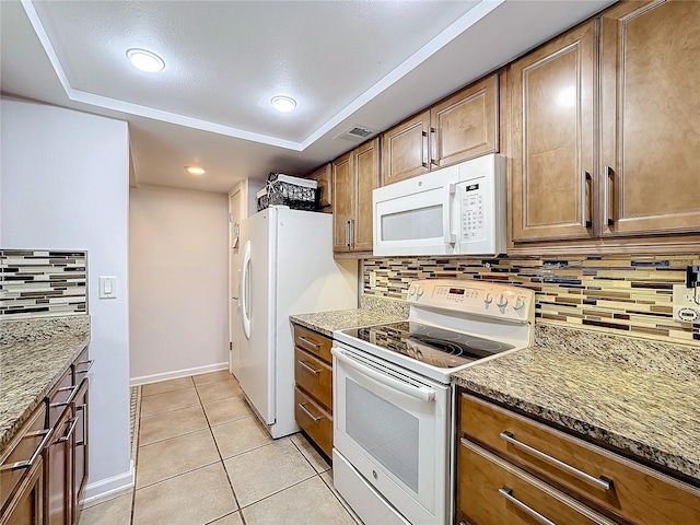 kitchen featuring tasteful backsplash, stone countertops, light tile patterned floors, a raised ceiling, and white appliances