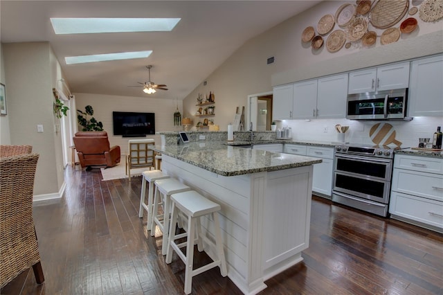 kitchen featuring a breakfast bar, a peninsula, appliances with stainless steel finishes, a skylight, and dark wood-style flooring