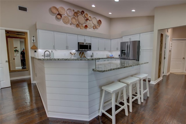 kitchen featuring a peninsula, light stone counters, visible vents, and stainless steel appliances