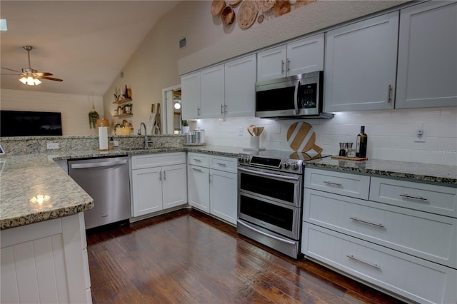 kitchen with vaulted ceiling, light stone countertops, appliances with stainless steel finishes, and a sink