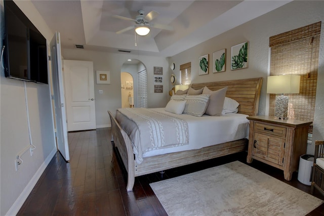 bedroom featuring visible vents, a tray ceiling, arched walkways, baseboards, and dark wood-style flooring