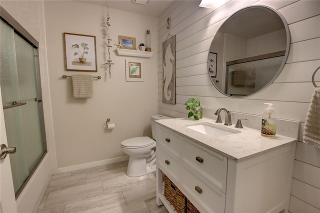 bathroom with toilet, baseboards, wooden walls, enclosed tub / shower combo, and vanity