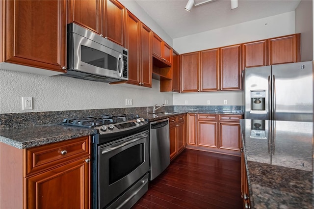 kitchen with dark wood-type flooring, appliances with stainless steel finishes, sink, and dark stone counters