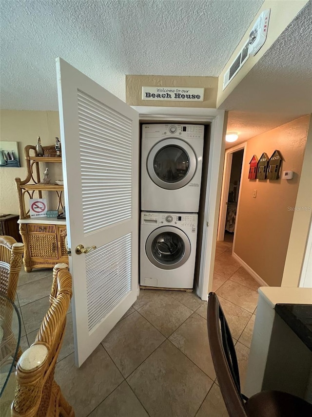 clothes washing area featuring tile patterned flooring, stacked washer / drying machine, and a textured ceiling