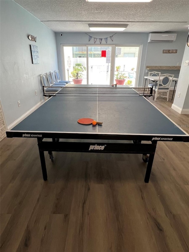 game room with wood-type flooring, an AC wall unit, and a textured ceiling