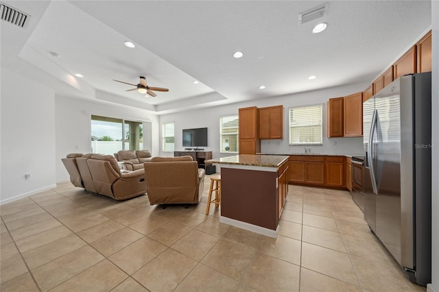 kitchen featuring a breakfast bar, light tile patterned floors, a tray ceiling, stainless steel fridge, and a kitchen island