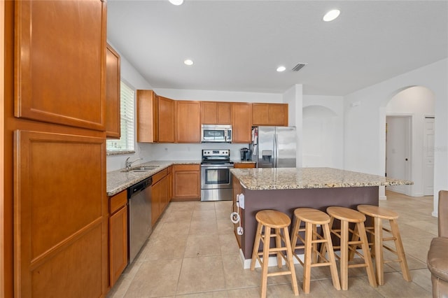 kitchen featuring light tile patterned flooring, a kitchen bar, sink, appliances with stainless steel finishes, and a kitchen island