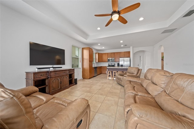 living room featuring light tile patterned flooring, ceiling fan, and a raised ceiling