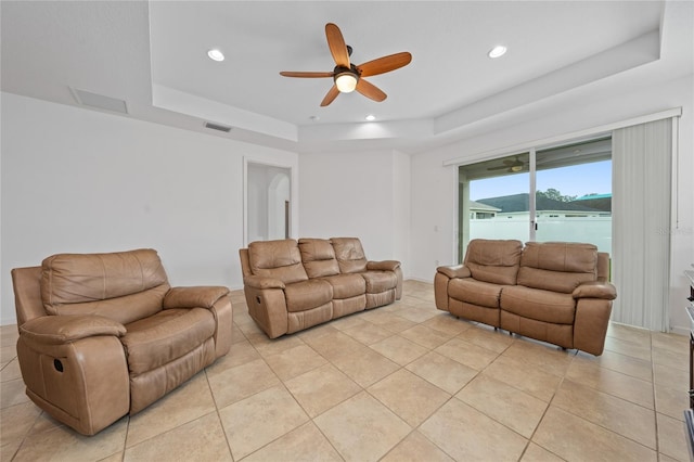 tiled living room with a water view, ceiling fan, and a raised ceiling