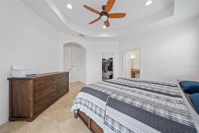 tiled bedroom featuring ceiling fan, a walk in closet, a raised ceiling, and a closet