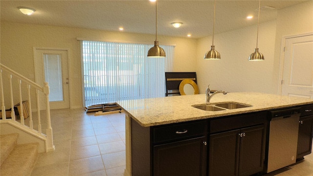 kitchen featuring decorative light fixtures, an island with sink, sink, stainless steel dishwasher, and light stone countertops